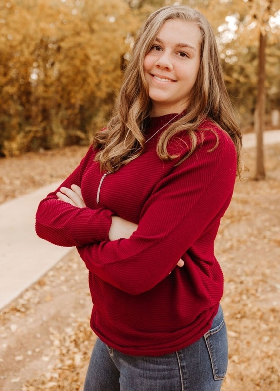 A teen girl in a red top with her arms crossed poses for a photo alongside a sidewalk.