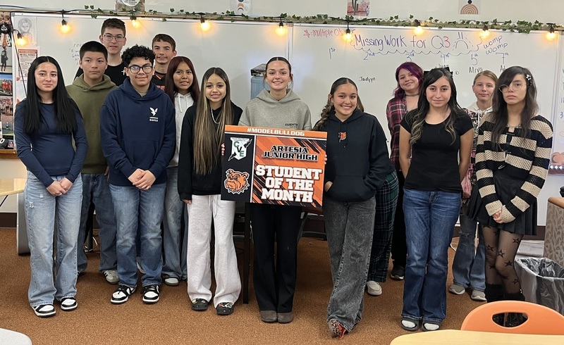 A teen girl surrounded by other teen students holds a sign that reads "Student of the Month".