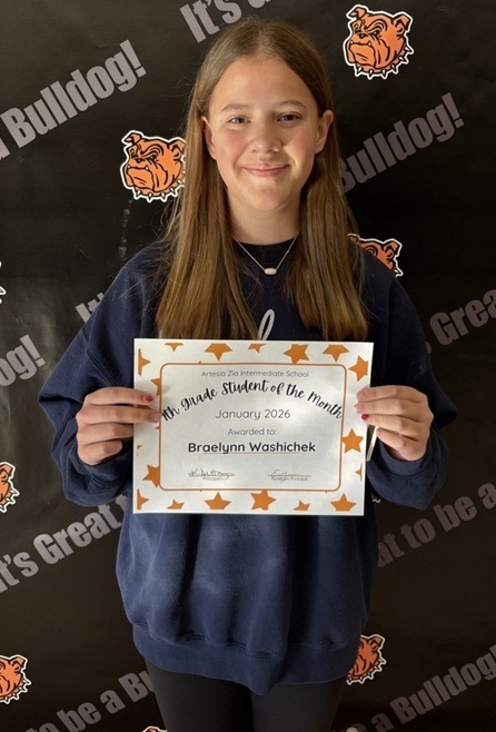 A teen girl in a grey long-sleeved sweatshirt holds a sign reading "Seventh-Grade Student of the Month".