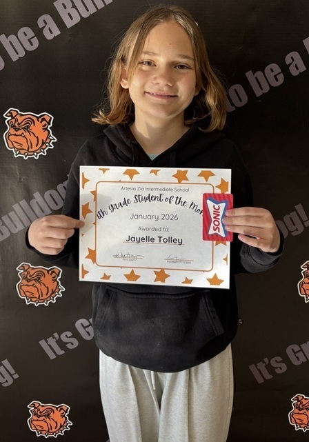 A teen girl in a black sweatshirt and grey sweatpants holds a certificate reading "Sixth-Grade Student of the Month".