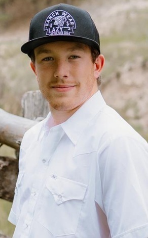 A teen boy in a white dress shirt and black baseball cap poses for a photo.