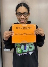 A teen boy in a black shirt and glasses holds an orange sign reading "Student of the Month".