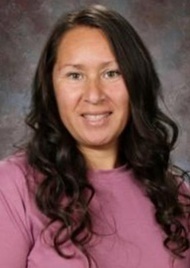 A female teacher in a purple top poses for a photo.