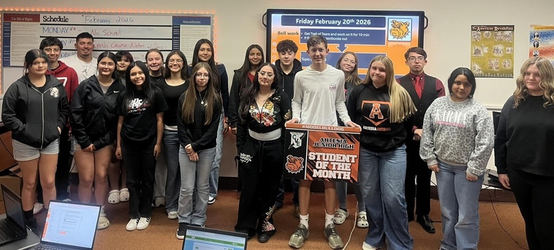 A tall teen boy surrounded by other teens holds a sign reading "Students of the Month".