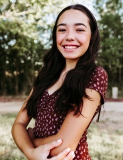 A teen girl in a printed top poses for a photo outdoors.