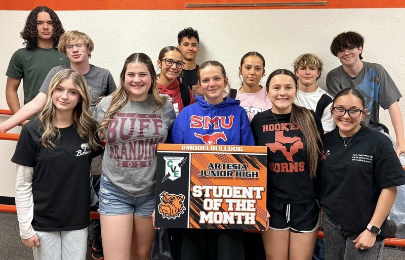 A teen girl in a blue SMU sweatshirt surrounded by other teens holds a sign reading "Student of the Month".