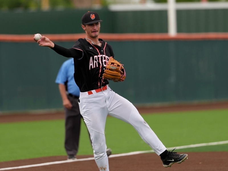 A teen boy in a black, white and orange baseball uniform prepares to throw from his right hand from third base.