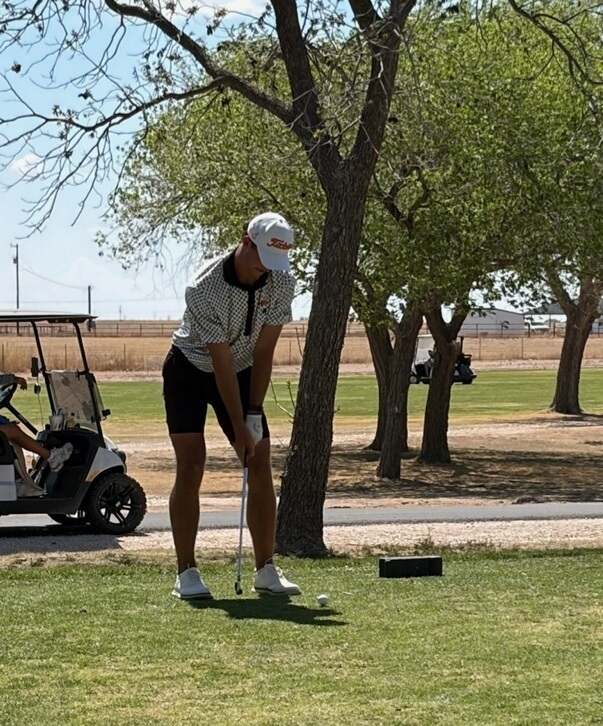 A teen boy in golf clothes lines up his shot in a tee box.