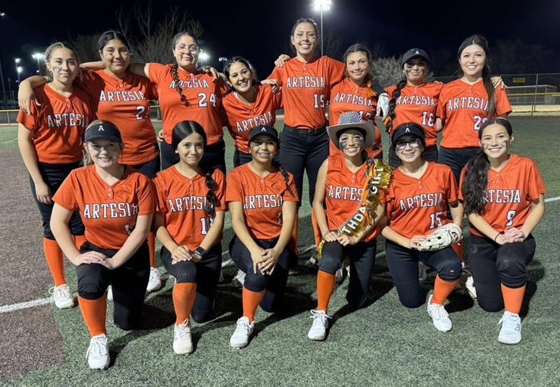 A girls' softball team in orange and black uniforms poses for a photo.