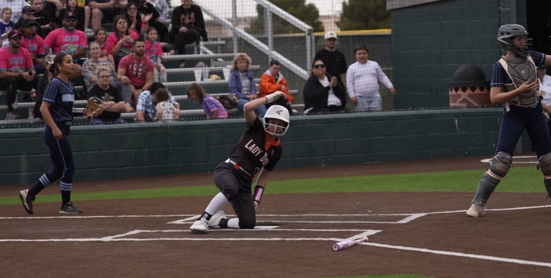 A teen girl in a black and orange softball uniform slides into home plate.