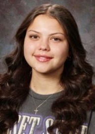 A teen girl with long dark hair and a grey top smiles for the camera.