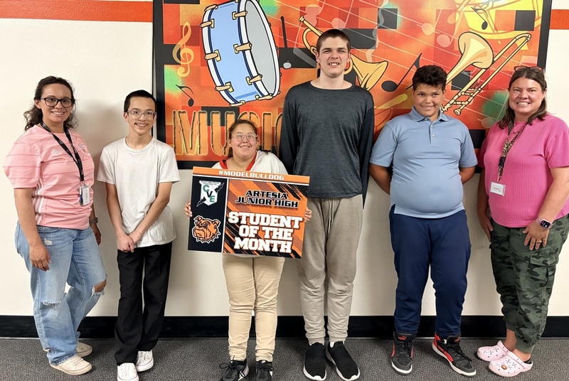 A teen girl surrounded by other teens and a female teacher holds a sign reading "Student of the Month".