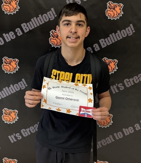 A teen boy in all black holds a sign reading "Seventh-Grade Student of the Month".