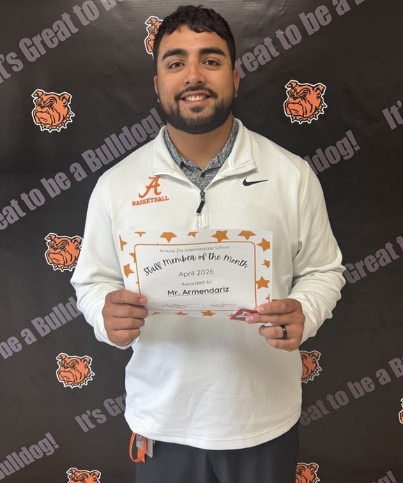 A male teacher in a white athletic top holds a certificate reading "Teacher of the Month".