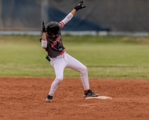 A teen boy in a black and orange baseball uniform gestures from second base.