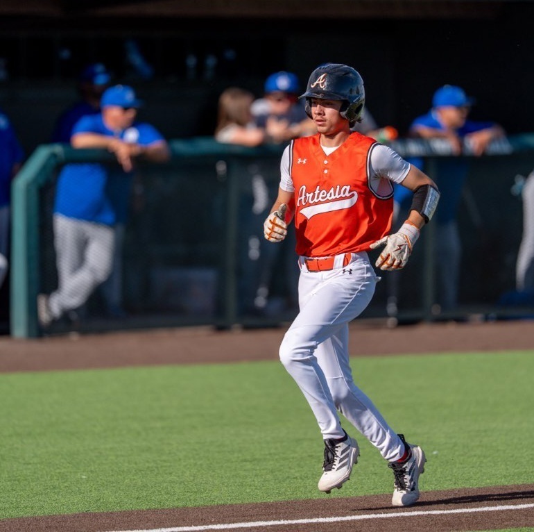 A teen boy in an orange and white baseball uniform runs down the third-base line.