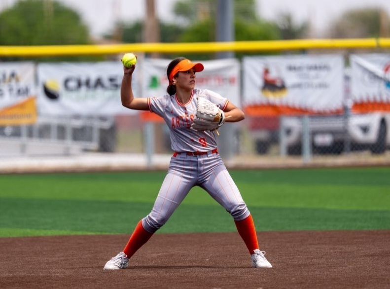 A teen girl in a grey and orange softball uniform prepares to throw the ball to first base from second.