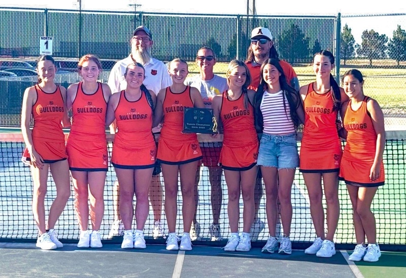 A high school girls' tennis team in orange and black uniforms poses for a photo with a plaque.