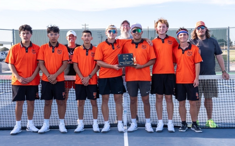 A high school boys' tennis team in orange and black uniforms poses for a photo with a plaque.