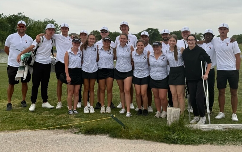 High school boys' and girls' golf teams in white and black uniforms pose for a photo near a sand trap.