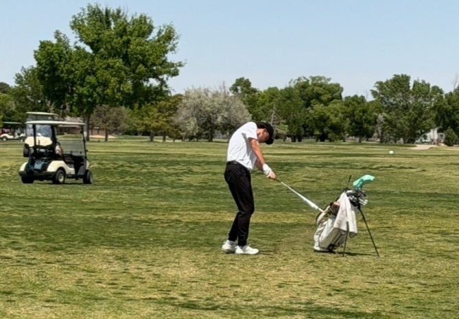 A teen boy in white and black prepares to hit a ball from the fairway.