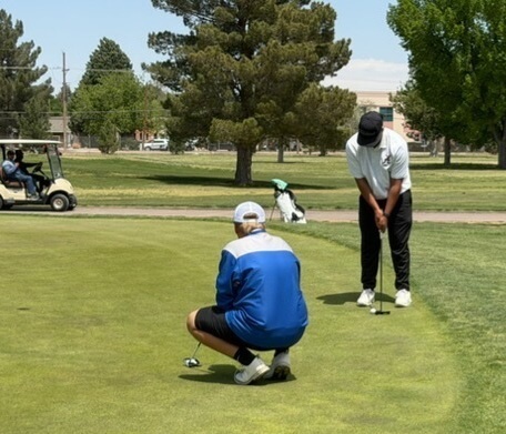 A teen boy in white and black lines up his putt as an opponent in blue looks on.