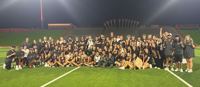 A large group of male and female teens and several male and female coaches pose for a photo on a football field.