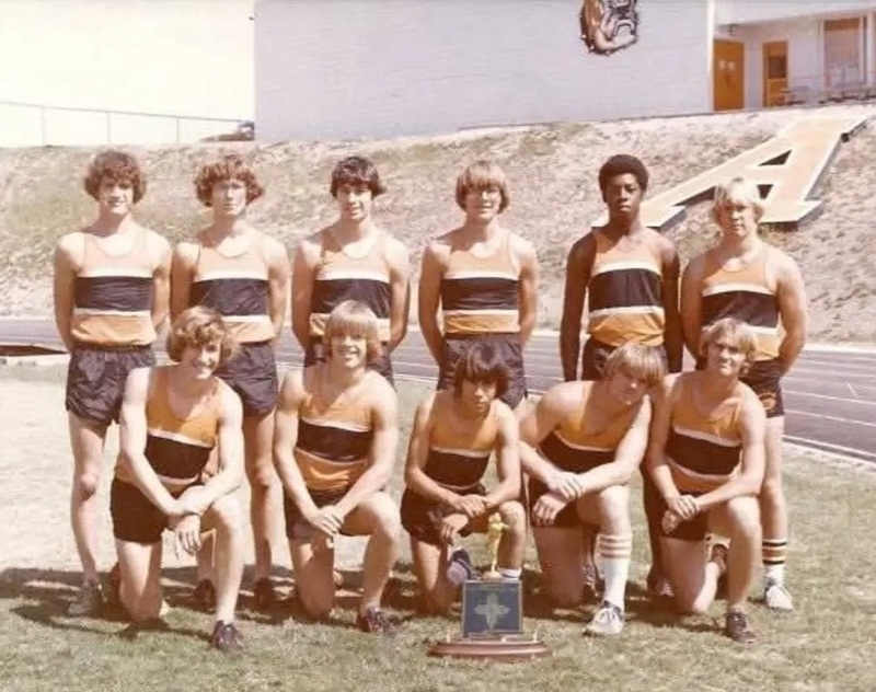 Eleven teen boys in orange, black and white track uniforms pose for a photo.