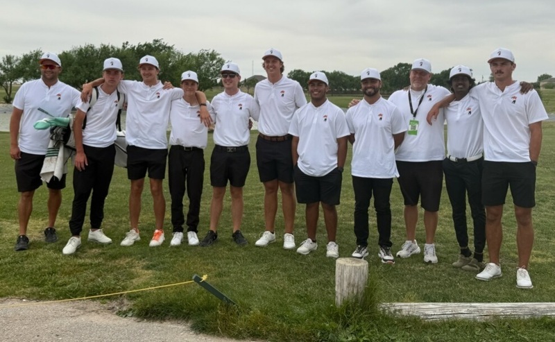 A group of teen boys in white and black golf uniforms pose for a photo on a course.