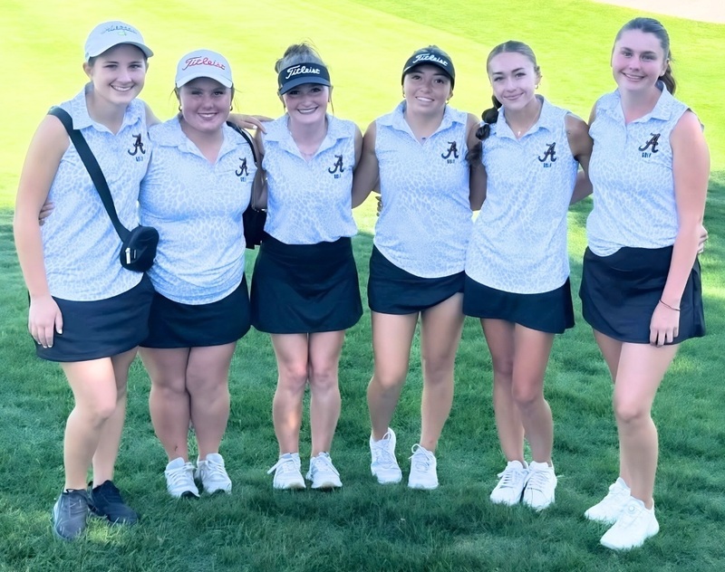 Six teen girls in white and black golf uniforms pose for a photo.
