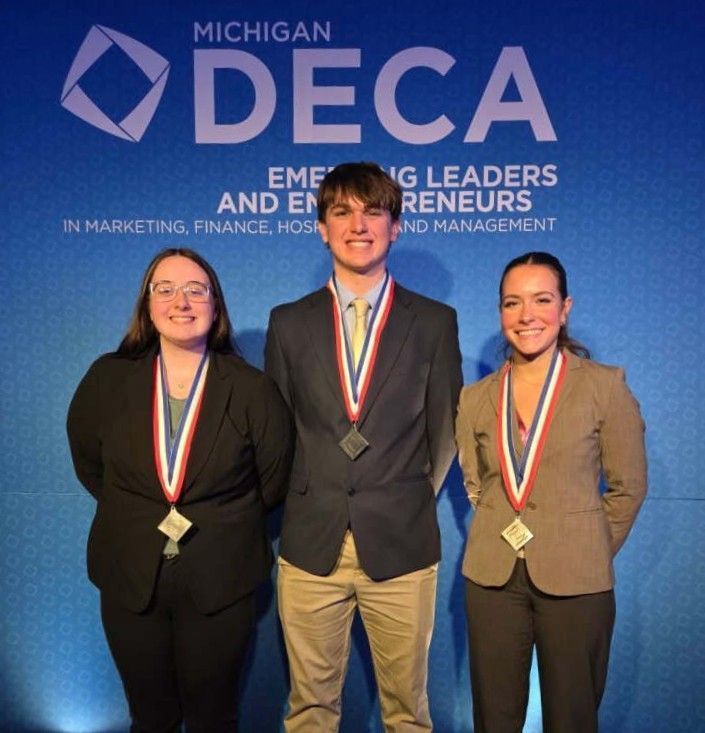 Three people are lined up wearing DECA medals against a blue background featuring the blue DECA logo