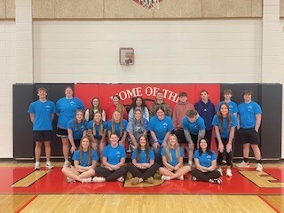 FBLA members posing in their blue club t-shirts during FBLA week. They are posing in the high school gymnasium.