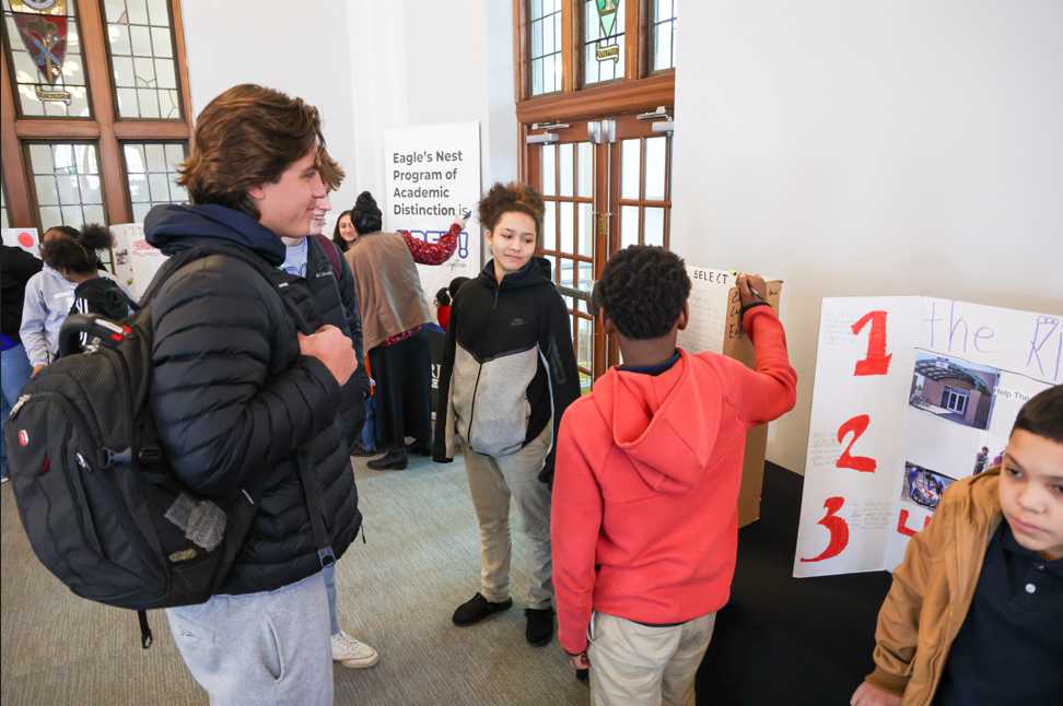 Students talking about their project to an individual in front of their tri-fold.