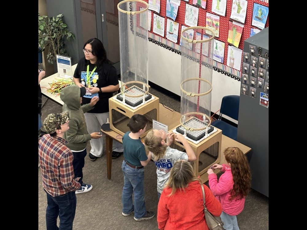 Students participate in a hands-on science experiment with a staff member at a science  station.