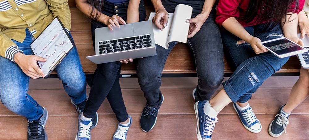 Students sitting on bench with computers and notebooks
