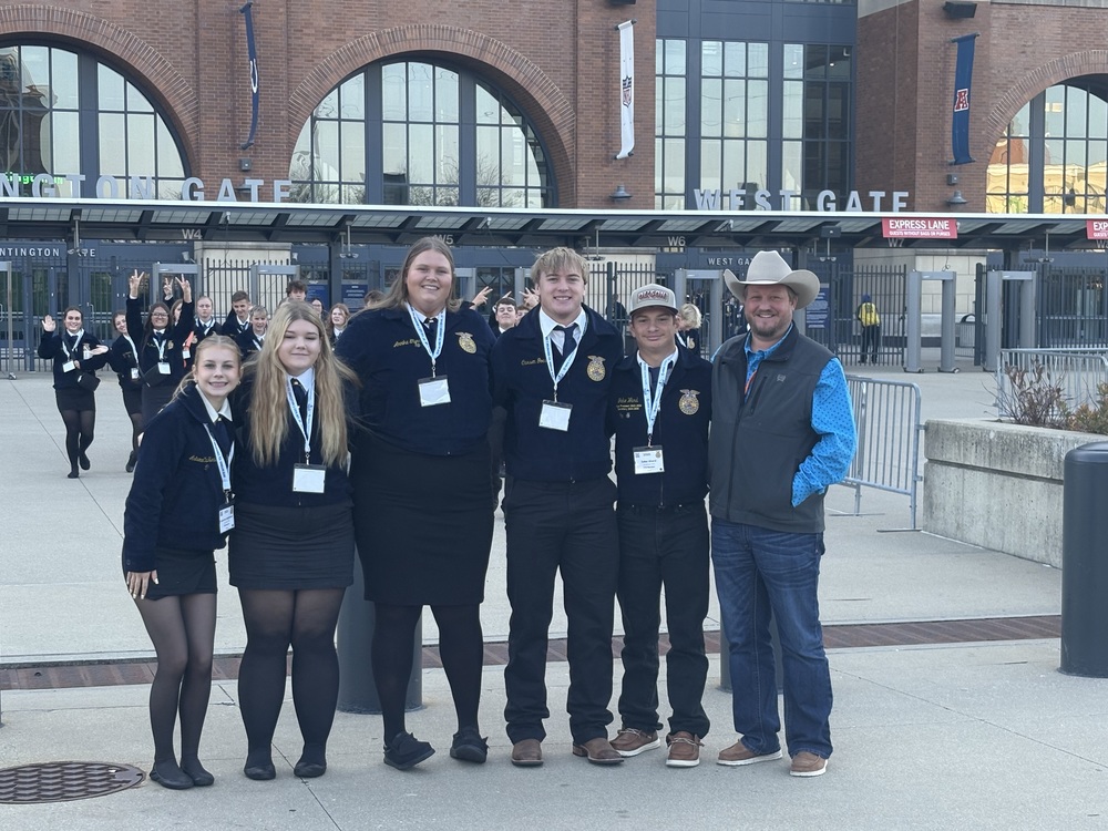Five Southern FFA members and their advisor pose together outside a large arena entrance labeled “West Gate.” The group is dressed in official FFA attire, smiling, with additional FFA students walking in the background.