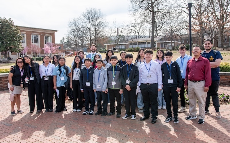 a group of school aged students standing in a courtyard, with brick buildings in the background