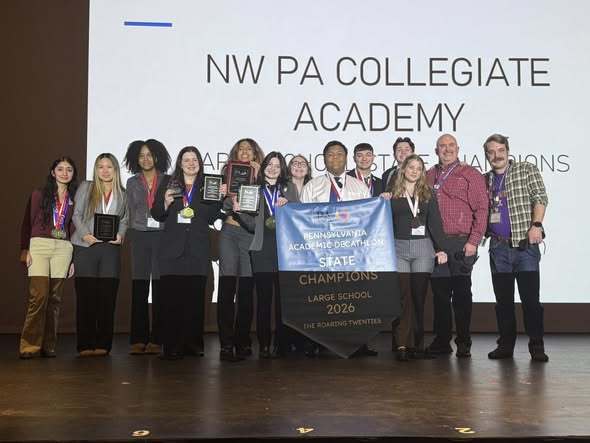  Students and staff on stage smiling while they hold their awards.