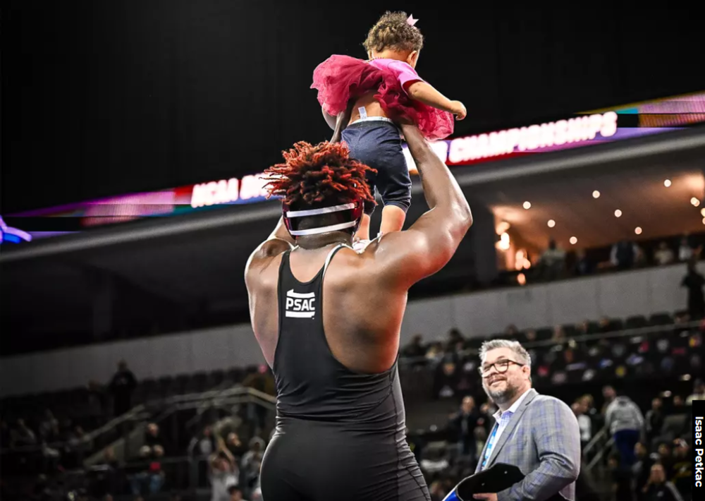 A wrestler holding his baby up after he won. 