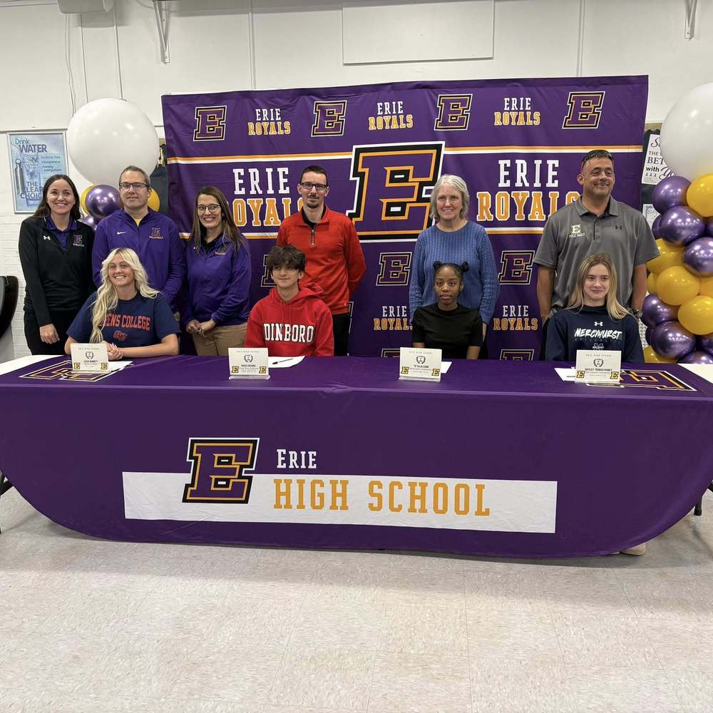 People standing and sitting behind a long table with a purple table cloth on it that says Erie High School.