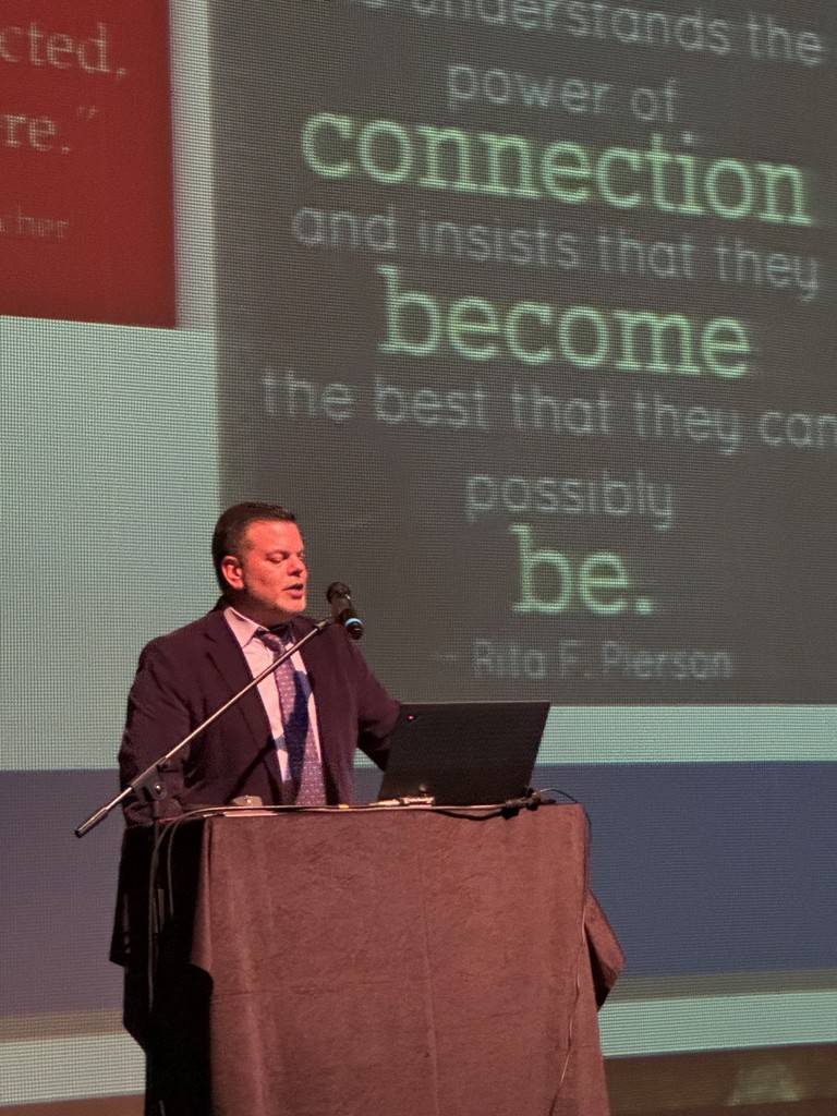 Superintendent Hattrick standing on stage delivering welcoming the staff back for the 2025-26 school year