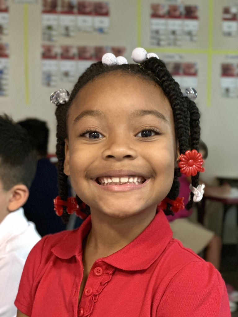 A young girl with braids and red shirt smiling for camera