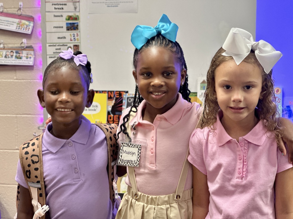 Three young girls with bows in their hair smile at camera.