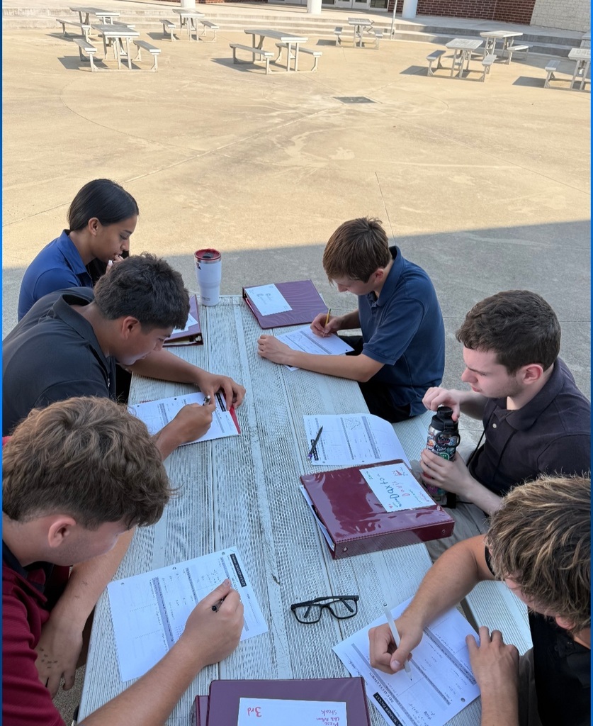 A group of students sitting outside on a sunny day, working together on math activities at tables