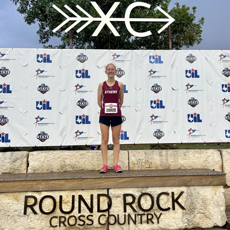 The photo of Donna standing in her racing attire on a stone stage it says round rock cross country