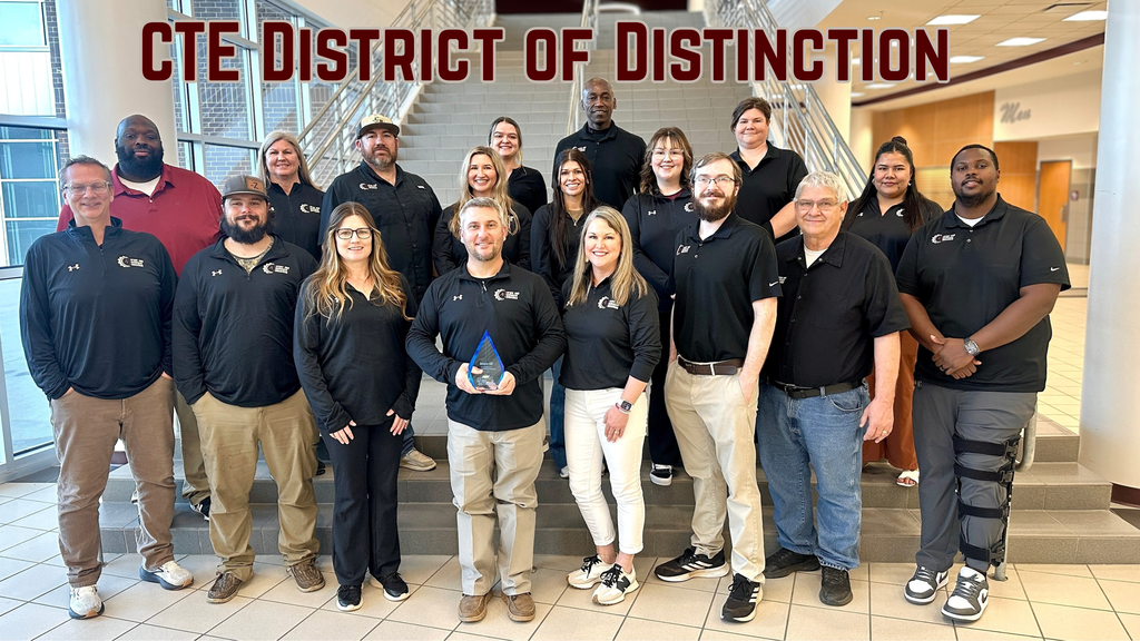 Group photo of Athens ISD Career and Technical Education staff standing on a wide indoor staircase inside a school building, wearing black Athens ISD CTE shirts. One staff member in the front center holds a glass award recognizing the district as a CTE District of Distinction.