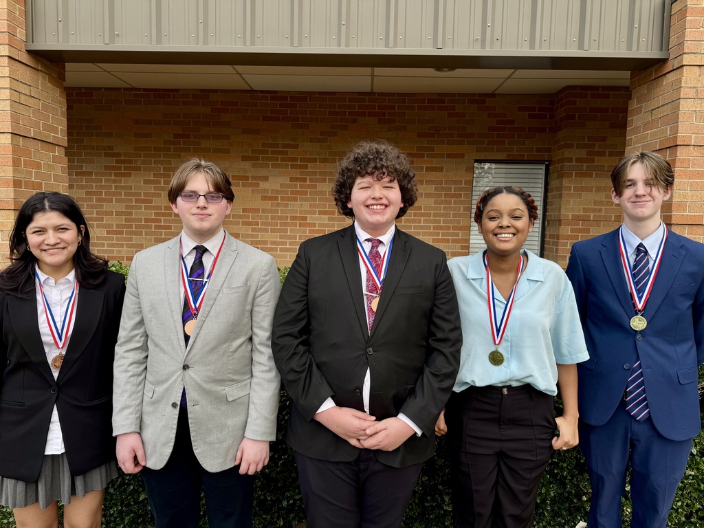 Five Athens High School debate students stand side by side outside in front of a brick building, each wearing a medal around their neck. The students are dressed in formal attire, including suits, ties, and blazers, and are smiling at the camera
