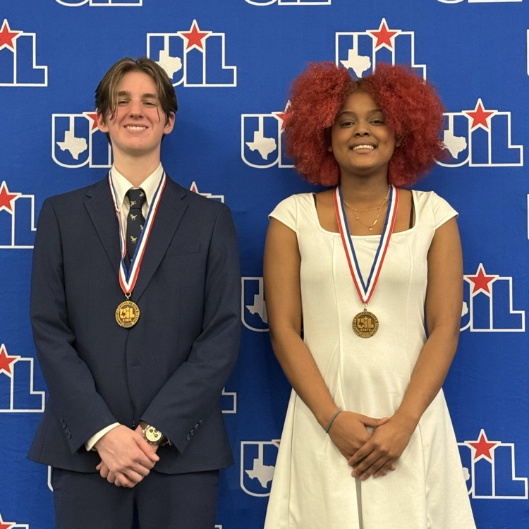 Photo of a young man in a suit next to a young lady in a white dress. They both have meds around their neck. They’re standing in front of a background that says UIL