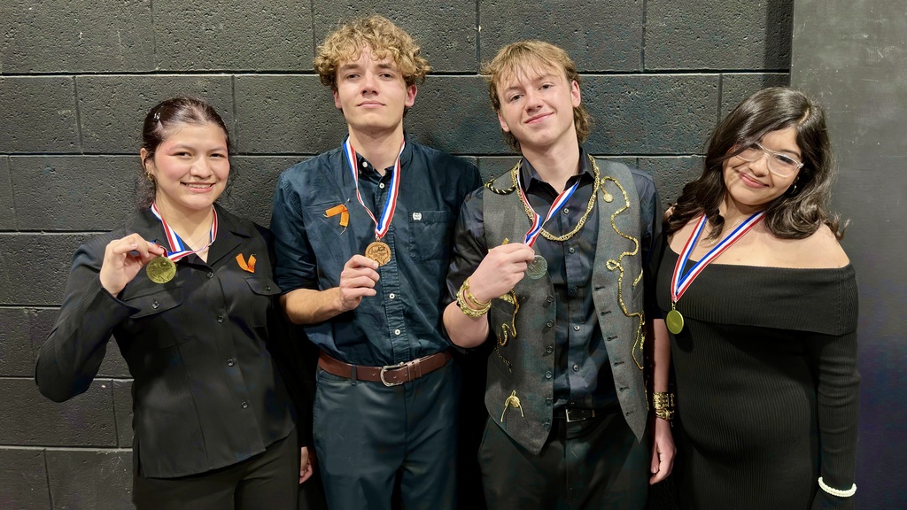 Four Athens High School theatre students stand side by side against a dark wall, each wearing a medal and smiling at the camera. From left to right: a student in a black button-up shirt holding a gold medal, a student in a dark outfit with a bronze medal, a student in a black shirt and decorative vest holding a medal, and a student in an off-the-shoulder black dress wearing a gold medal.