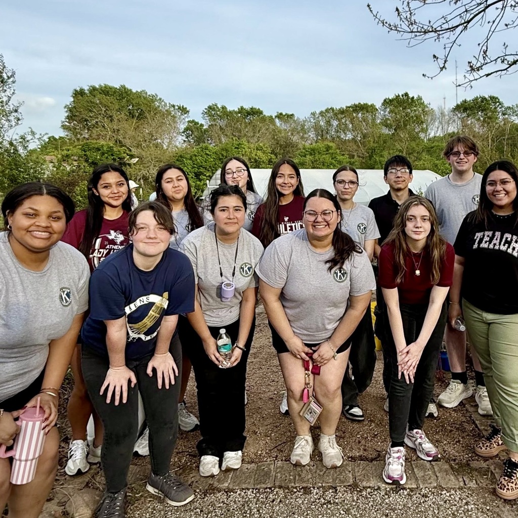 A group of Athens High School students and their advisor pose together outdoors at the East Texas Arboretum’s Dream Garden, smiling and standing on a gravel path with greenery and garden structures in the background after helping with a spring cleanup.